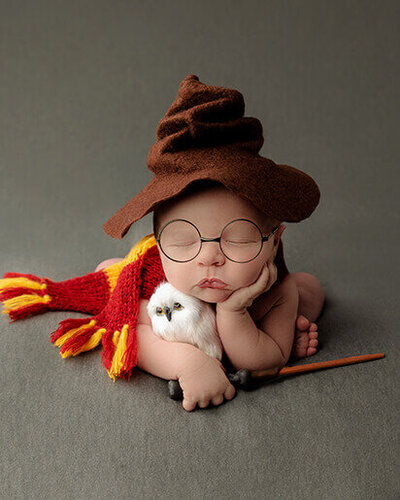 A baby in the froggy pose dressed like Harry Potter.