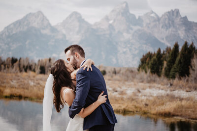 grand teton wedding with bride and groom holding each other in front of the Tetons and kissing each other passionately captured by jackson hole photographers
