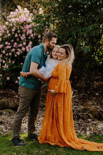 Dad kissing his daughter which holding her. Mom is holding the daughter from the other side.