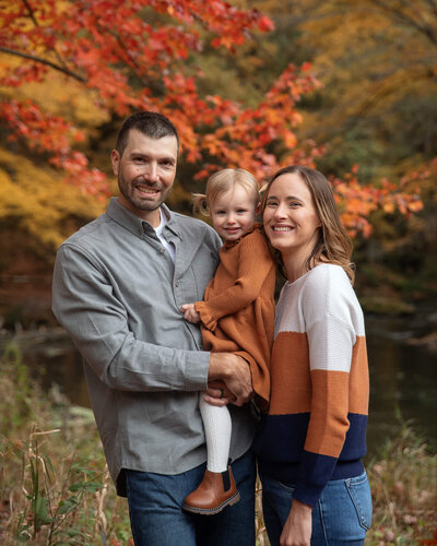 Dad and Mom with their toddler girl on a colorful fall afternoon.