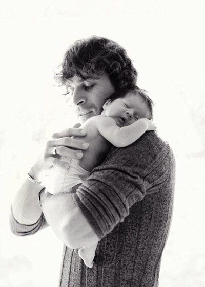 San Francisco Bay Area natural newborn photographer captures black and white photo of dad holding newborn baby by window.