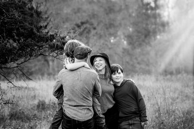 Mother is looking at her youngest son, who is held by his father, lovingly while the oldest boy is looking at the camera with a smile