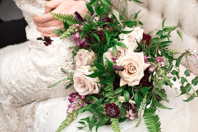 Detail photo of pink and purple bouquet with greenery beside bride on couch