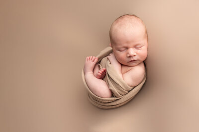 Newborn baby wrapped in brown wrap on brown blanket