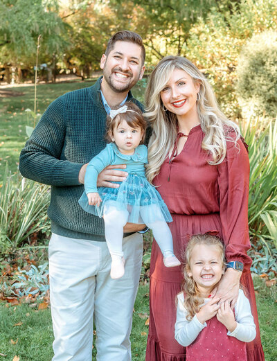 Professional family photography by Stamford CT photographer showcasing parents with two young daughters in coordinated fall colors in beautiful outdoor park setting
