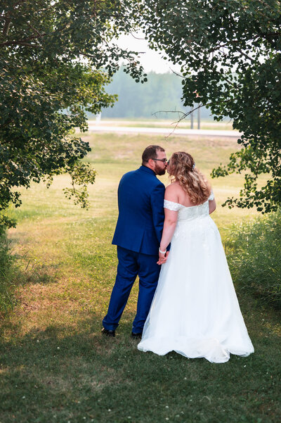 Bride and groom kiss in treed archway at their wedding in Alberta