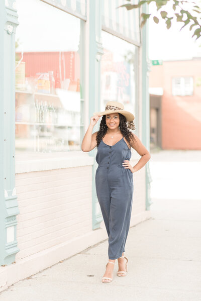 senior girl walking down the sidewalk in ludington with her hand on her hat