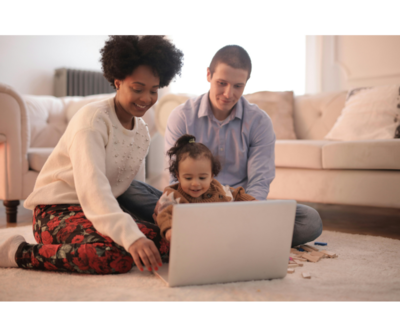 A woman, man and baby sitting on the ground with a laptop in front of them