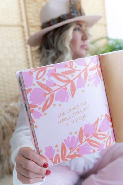 Book on divorce coaching services, featuring a pink cover with floral print, held by a coach in a stylish white outfit and hat. This guide is designed to support individuals through the challenges of divorce with professional and compassionate advice.