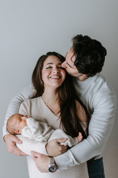 Newborn Photographer, Husband kissing wife's head while she holds newborn baby