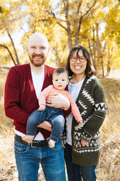 Two parents smiling while holding their child in between them.