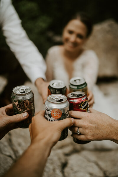 Bride and friends toast with beers during casual outdoor wedding in Breckenridge.