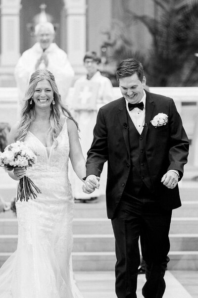 bride and groom walking down the aisle of a church while holding hands