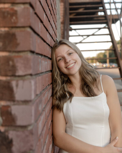 Senior girl leaning up against a brick wall. Metal staircase in the background.
