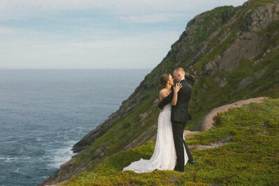 bride and groom embrace beside a dramatic sea cliff