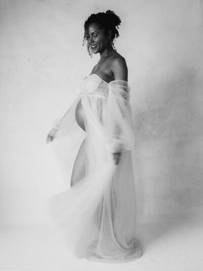 maternity session sitting in lounge chair in tight white dress