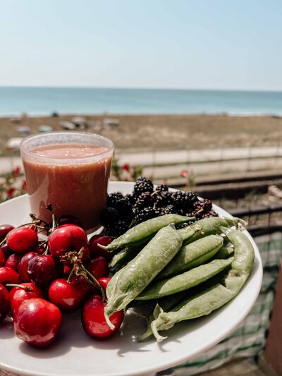 Healthy plate of cherries, green beans, and blackberries, accompanied by a smoothie, with a serene ocean view in the background, showcasing a balanced and intuitive diet.