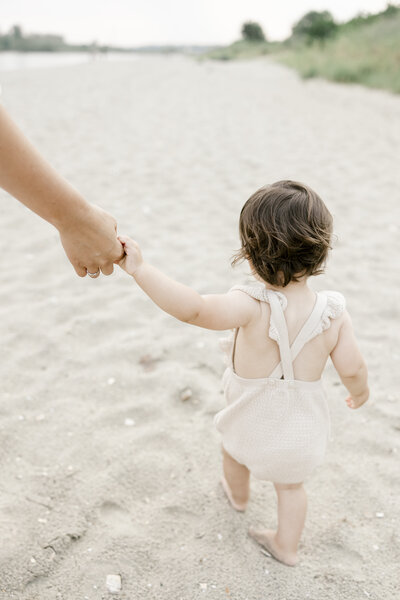 Mother holding her baby girl's hand while walking on the beach