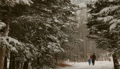 Engaged couple running away from the camera in a snowy forest.