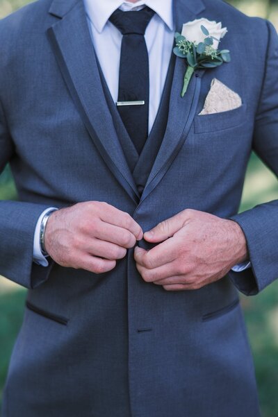 close up of groom buttoning suit jacket