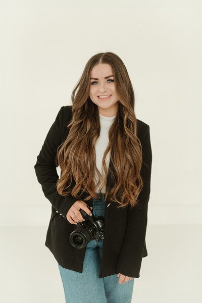 Branding photo for Bailee Freeman Photography with a black blazer and a Nikon camera in front of her. 