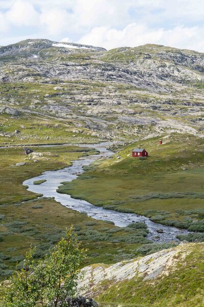 A red norweigan cabin in the middle of the wilderness next to a beautiful river.