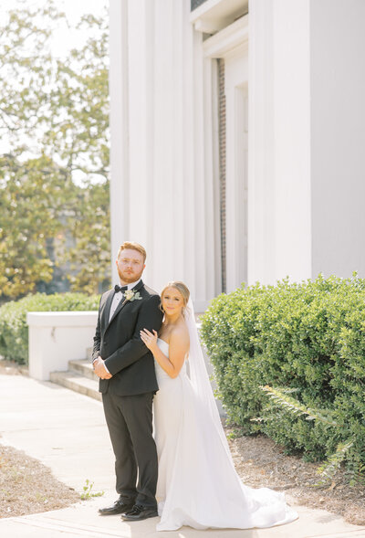 bride holding groom's arm in front of a building with white columns