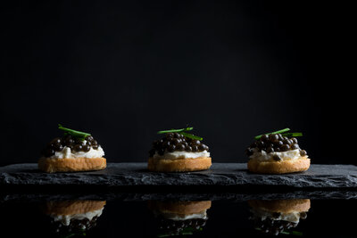 Three caviar appetizers in an aligned row on a black textured background