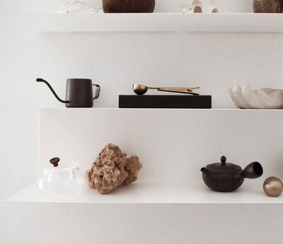 white floating shelves with black mug, black box with gold spoon, black bowl, piece of brown coral