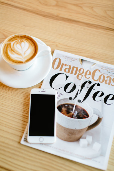 Mug of coffee magazine and phone on a wood table