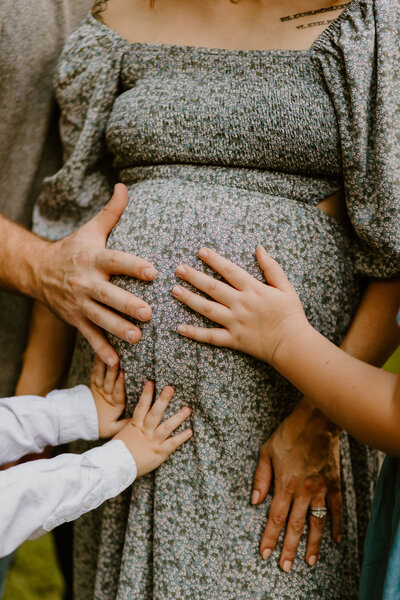 family placing hands on mom's baby bump