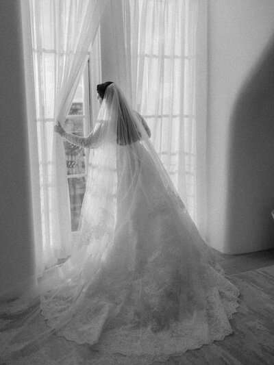 A bride peers out a window at her museum wedding.