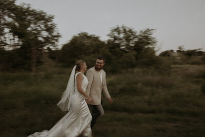 Blurred photo of husband and wife running across a field on their wedding day.
