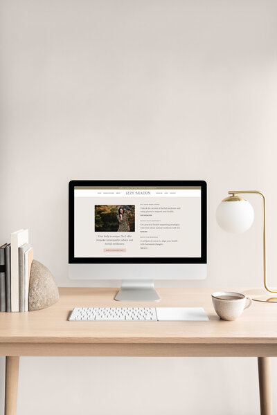 Desktop computer displaying Izzy Seadon’s website with information about naturopathic advice, herbal medicines, and health courses, placed on a desk with a lamp and a cup.