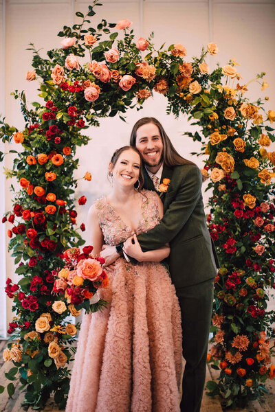 Couple on their wedding day at The Tinsmith in Madison standing in front of a floral arch by Briar Loft.