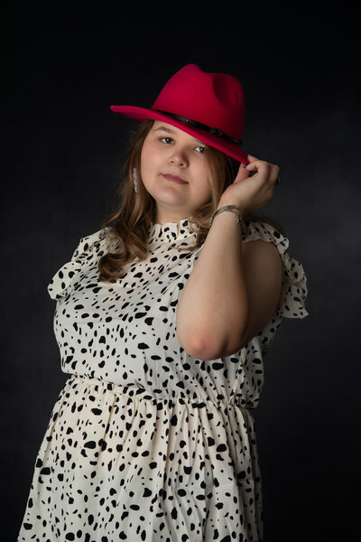 senior-in-studio-wearing-red-fedora-hat-and-white-and-black-pattern-dress-in-arlington-tx