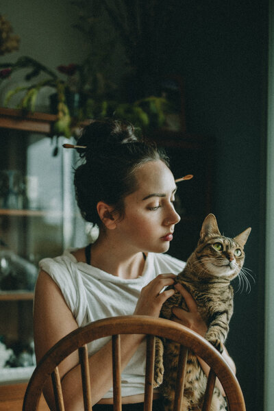 white woman with brunette hair tied up in a bun holds her cat. She is wearing a white shirt with rolled-up sleeves.
