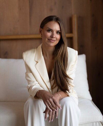 Female taking a branding photoshoot, sitting down wearing a white suit with long brown hair
