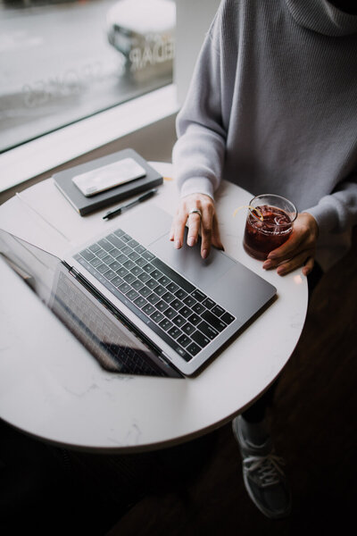Hailey Ann Co Bookkeeper and somatic money coach for female entrepreneurs sitting at a table with iced coffee, laptop and notebook