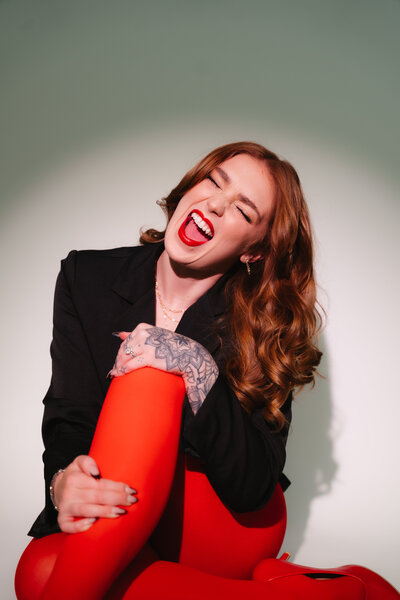 Makall laughing with bright red pants and black top — playful bridal artist portrait inviting contact