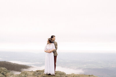 Cinematic wide shot of the couple embracing on the summit, with soft focus and natural light.
