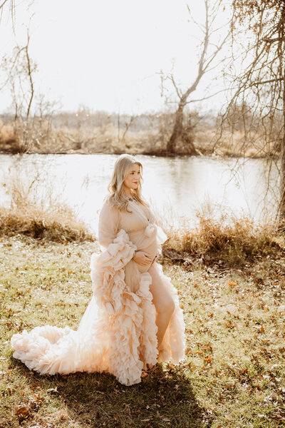 Pregnant mom stands in an elegant dress holding her belly while smiling into the distance.