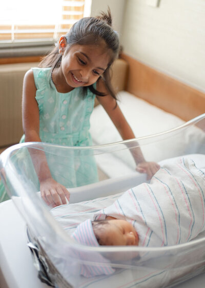 Little girl looking down at baby brotherin hospital bassinet during newborn session at Northside Hospital Atlanta.