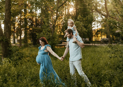 mom holds dad's hand during maternity photoshoot in elkhart indiana and leads him and daughter