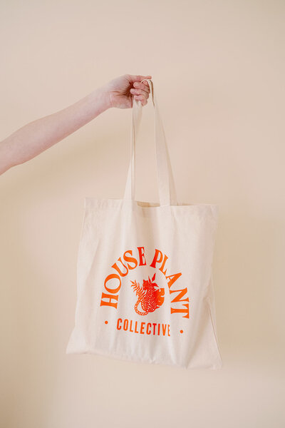Hand holding a canvas tote bag with the House Plant Collective logo on it