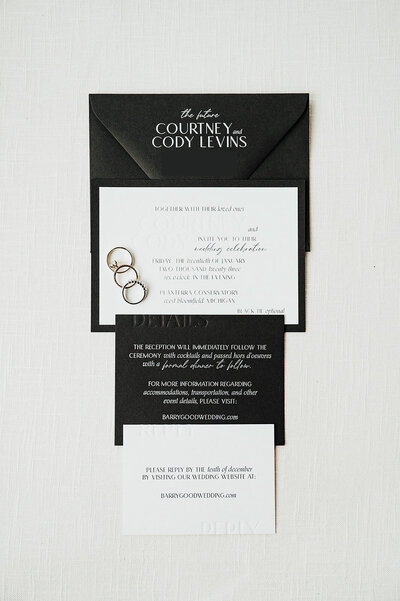 A black and white custom wedding invitation suite featuring a debossed invitation with wedding rings on it and a details and RSVP card by alyssa amez design custom wedding stationery and signage designer against a white background.
