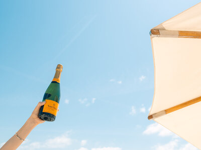 Arm holding champagne bottle in the air next to a beach umbrella