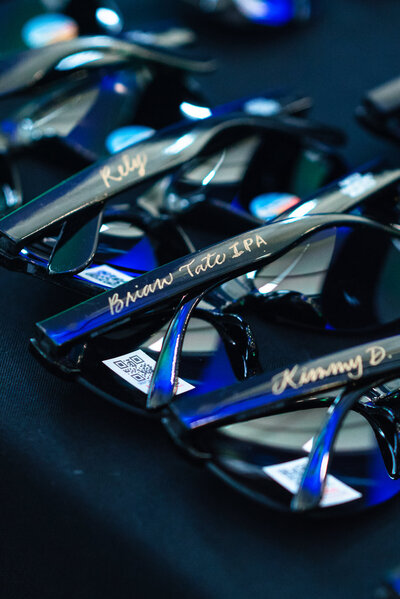 Close-up of custom conference sunglasses with handwritten names, photographed at a corporate event at the Dubois Center in Charlotte, NC by DeLong Photography, a Charlotte event photographer.