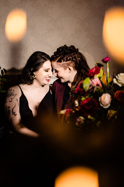 Two brides smiling with their foreheads touching surrounded by gothic-inspired wedding flowers