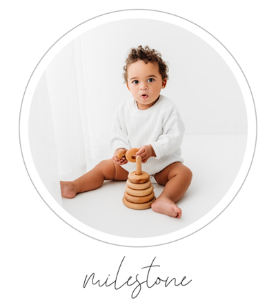 A portrait of a one-year old baby boy is captured on a white studio backdrop. He is playfully interacting with his wooden toys, creating a joyous atmosphere. The photographer, Bri Sullivan, skillfully captures the moment, highlighting the innocence and playfulness of the baby. This portrait commemorates the baby's milestone and showcases Sullivan's talent in capturing the essence of childhood.